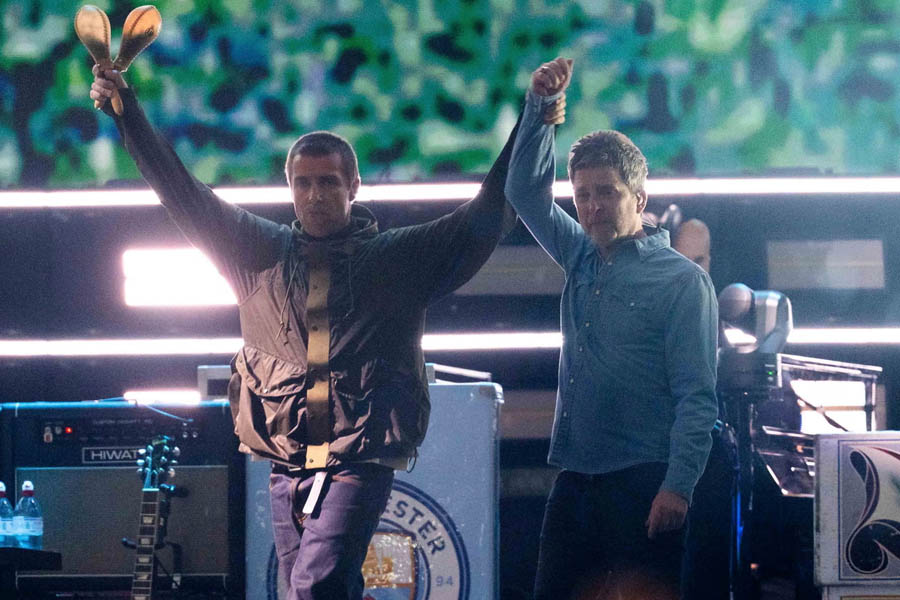Liam Gallagher (left) lifts the hand of his brother Noel Gallagher as Oasis perform their first reunion concert in Cardiff, July 2024 — marking a historic moment in the band’s comeback.