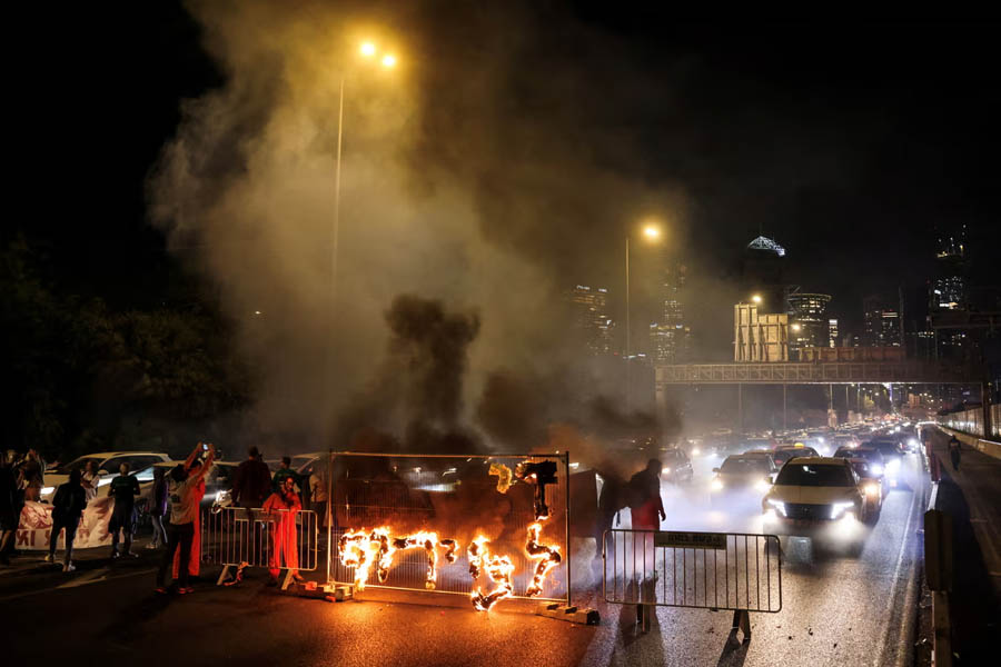 Fire blazes with the words in Hebrew, ‘Enough with the madness’, as demonstrators and relatives of hostages block a road in Tel Aviv