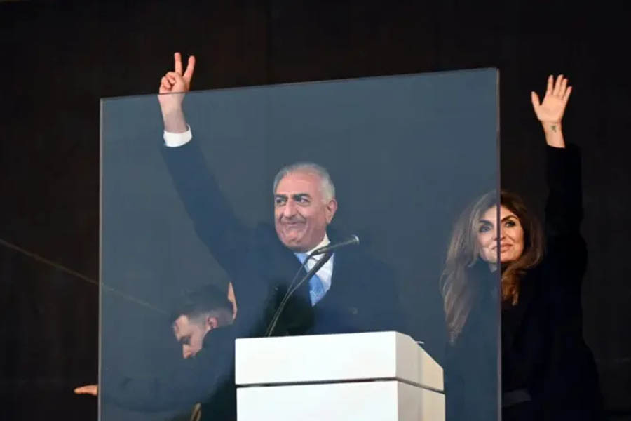 Reza Pahlavi and Yasmine Pahlavi greeting and waving at a crowd of supporters during a public rally event in Germany.